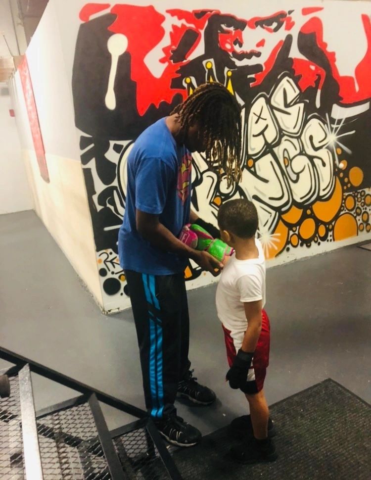 Coach working with a young boxer in front of the club mural